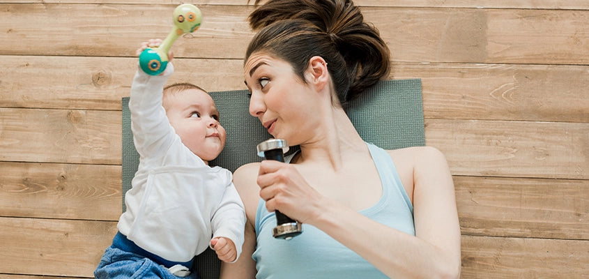 Frau liegt mit Hantel neben Baby