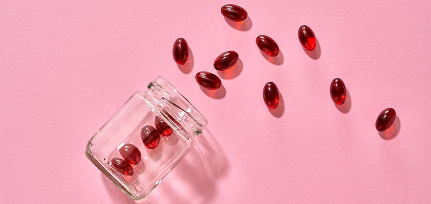 Astaxanthin: rote Pillen fallen aus Glas auf pinkem Hintergrund