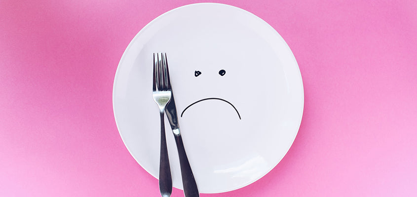 weißer Teller mit traurigem Smiley auf pinkem Hintergrund