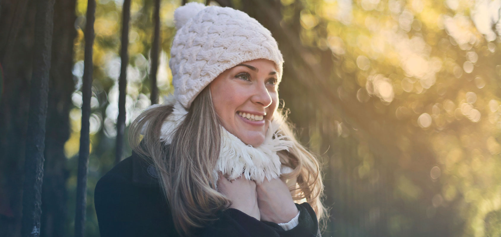 Lachende Frau mit Mütze und Schal im Wald