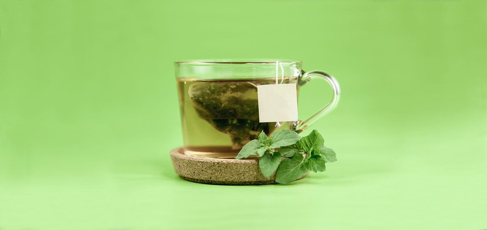 durchsichtige Tasse grüner Tee vor hellgrünem Hintergrund