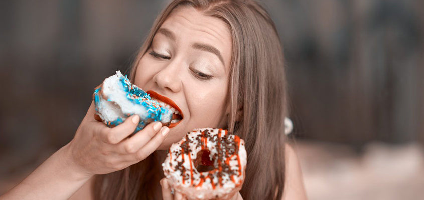 Frau isst zwei bunte Donuts gleichzeitig