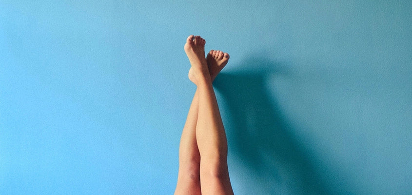 zwei nackte Beine hochgestreckt vor blauer Wand