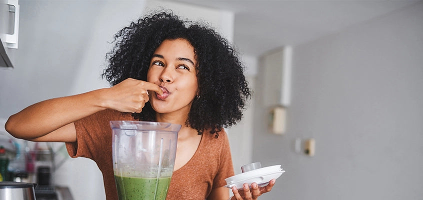 Frau probiert grünen Smoothie aus Mixer