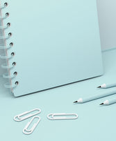 Hellblaues Notizheft, weiße Büroklammern und hellblaue Bleistifte auf hellblauem Hintergrund